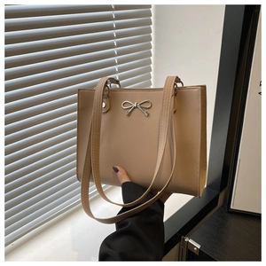Close-up of light brown tote bag with silver metal bow buckle and matte leather texture