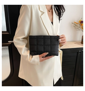 Detailopname van een zwarte gewatteerde clutch vastgehouden door een model in blazer