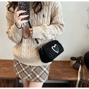 Détail du sac cylindre en peluche noire avec motif cœur blanc et boucles dorées