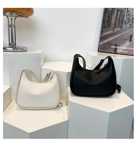 Close-up of crescent shoulder bags in black and cream with adjustable wide straps
