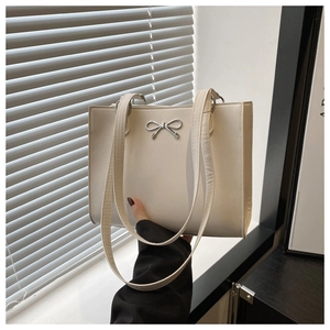 Detail of light beige tote bag with a sleek silver metallic bow and long shoulder straps
