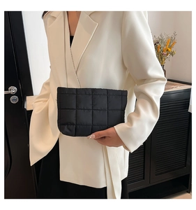 Detail van een zwarte gewatteerde clutch vastgehouden door model in witte blazer
