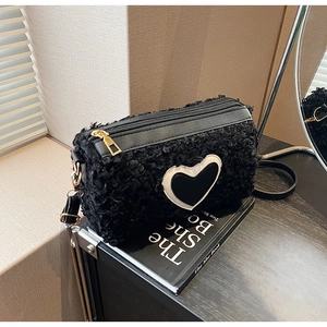 Détail du sac cylindrique en peluche noire avec écusson cœur blanc et fermeture éclair dorée