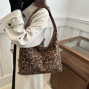 Chic leopard print hobo tote bag with brown leather strap worn by a woman in a trench coat