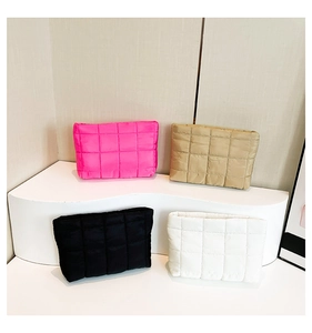 Gewatteerde make-up tassen in roze, kaki, zwart en wit op golvende displaystandaard