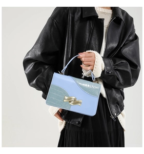 Detail of light blue crossbody bag with crocodile texture and wavy gold buckle