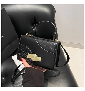 Detail of black crossbody bag with crocodile texture and golden metal buckle decoration