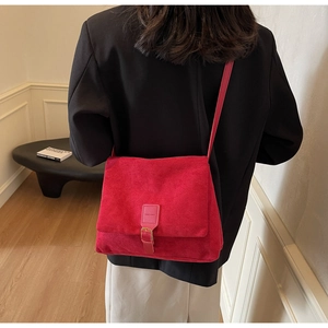 Red suede crossbody bag with gold buckle shown on a model in a minimalist setting