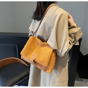 Detail of vintage ginger suede crossbody bag worn with a beige trench coat indoors