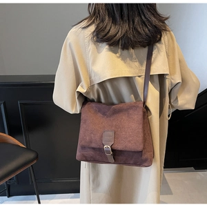 Detail view of dark coffee suede crossbody bag with leather strap on beige trench coat
