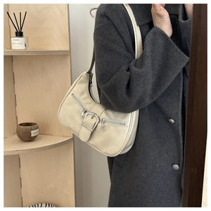 Détail du sac croissant crème avec poches zippées argentées et boucle sur l'épaule