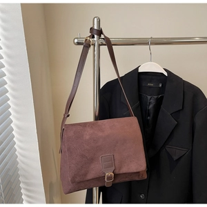 Detail of a dark brown suede crossbody bag featuring a classic rectangular flap and metal buckle