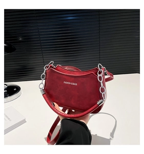 Close-up of wine red crescent bag with silver chain handle and white brand lettering