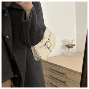 Détail du sac bandoulière croissant blanc cassé avec boucle argentée sur manteau