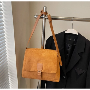 Detail view of tan suede crossbody bag with decorative buckle on a metal hanger