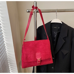 Detail of red suede crossbody messenger bag with flap closure on a metal hanger