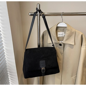 Close-up of matte black suede shoulder bag with gold buckle and adjustable strap detailing