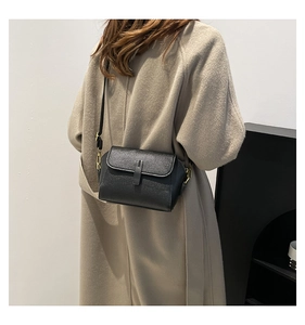 Détail d'un petit sac bandoulière en cuir noir texturé porté sur un manteau en laine