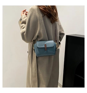 Détail du sac bandoulière en cuir grainé bleu avec fermoir marron et finitions dorées