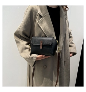 Sac à bandoulière en cuir noir classique avec détails dorés porté sur un manteau beige