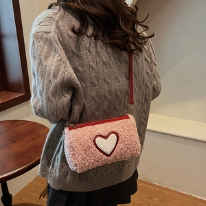 Sac cylindre en peluche rose avec détail cœur et bandoulière rouge sur pull gris