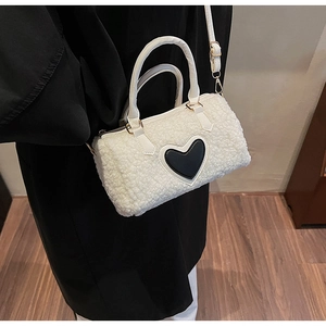 Detail view of white fleece cylinder bag featuring a black leather heart and top handles