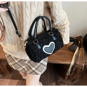 Detail of black faux shearling cylinder bag with heart patch on model with beige knitwear