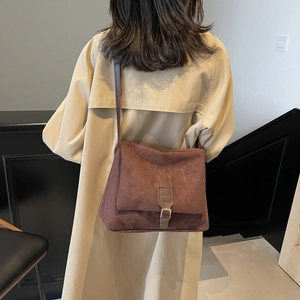 Brown suede shoulder bag with gold buckle worn with a beige trench coat