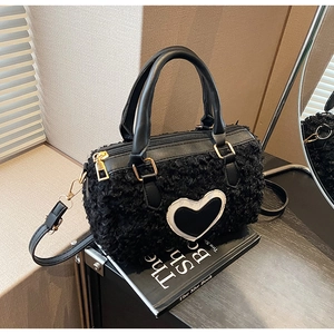Detail of black fuzzy cylinder bag featuring white-edged heart patch and gold hardware