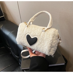 Close-up of white plush cylinder bag with black leather heart detail and gold hardware