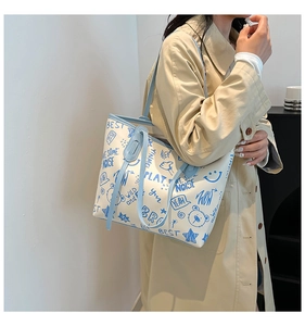 Vue latérale d'un grand sac cabas blanc avec graffitis bleus sur un trench-coat beige