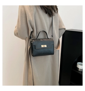 Detail of black cross-pattern leather crossbody bag with gold clasp on beige coat