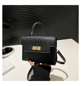 Detail of black cross-grain leather crossbody bag with elegant gold twist-lock closure