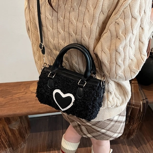 Black plush cylindrical bag with heart patch and golden hardware in a lifestyle setting