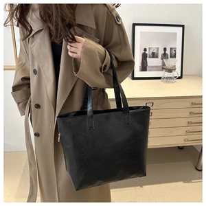Detalle de bolso tote negro con cremallera plateada llevado con una gabardina