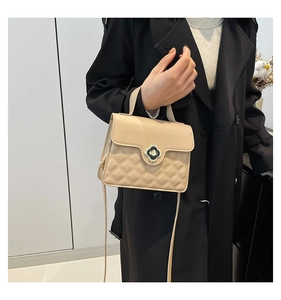 Detail of beige square handbag featuring quilted pattern and clover-shaped twist lock