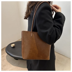 Brown leather tote bag worn over the shoulder showing the minimalist design and matte texture