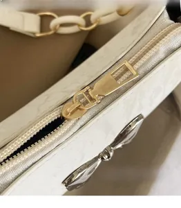 Detail of white embossed leather with gold zipper pull and silver bow decoration