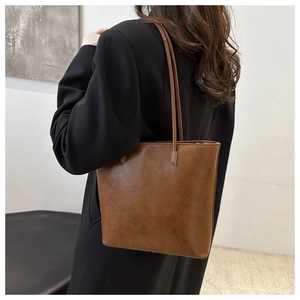 Close-up of a brown leather tote bag with vintage texture worn with a black wool coat