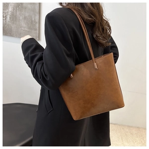 Brown vintage tote bag on model shoulder with black suit and minimalist interior