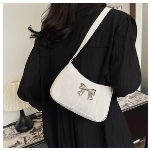 Detail of white crescent shoulder bag featuring a metallic silver bow and pleated texture