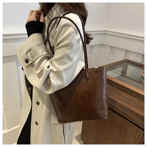 Detail of a deep brown glossy leather tote bag shown on model wearing a beige trench coat