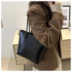 Classic black leather tote bag with long straps worn over the shoulder by a model