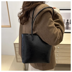 Chic black faux leather tote bag with long straps worn over the shoulder for daily commute