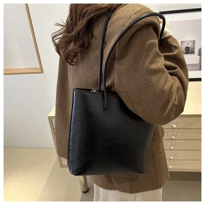 Detail of a black minimalist leather tote bag worn by a model in a cozy interior setting