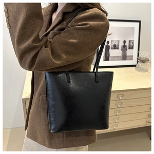 Close-up of a black leather tote bag worn by a model in a stylish brown tweed blazer