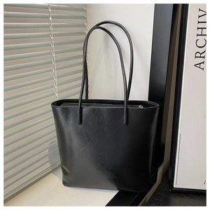 Detail of minimalist black tote bag in glossy finish with slender shoulder straps