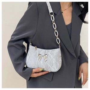 Detail of silver pleated crescent bag featuring a metallic bow and acrylic chain strap
