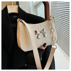 Close-up of white ruched leather crescent bag with silver bow buckle and chain strap