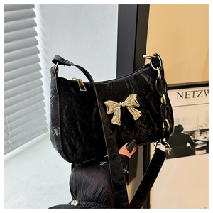 Detail of black crescent shoulder bag with golden bow and elegant textured finish